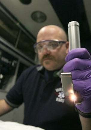 EMT with protective glasses and purple gloved hand holding an endotracheal tube