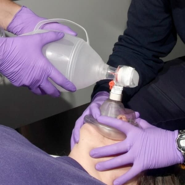 purple gloved hands holding a BVM over a patient's mouth