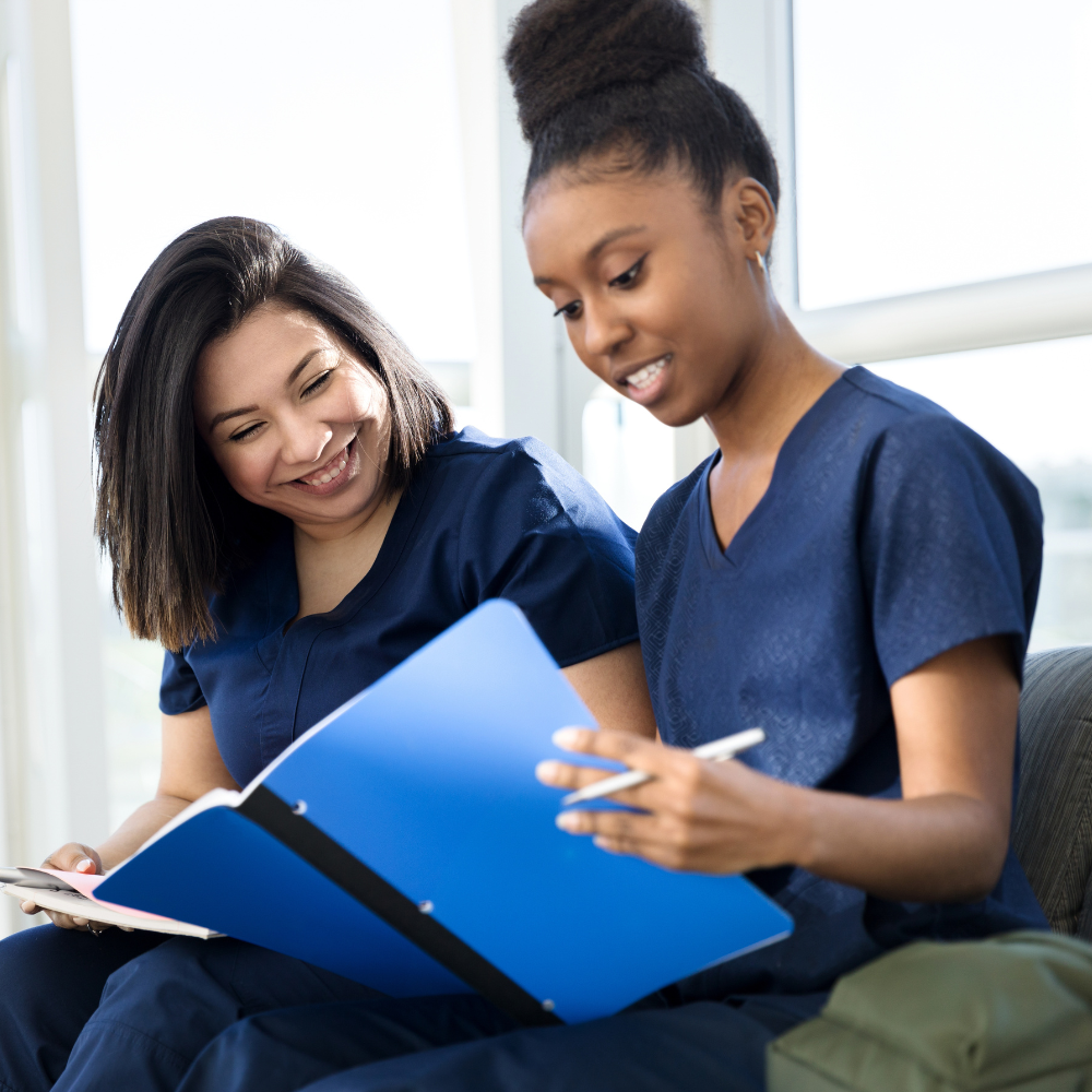 two adult female medical students look through a notebook together