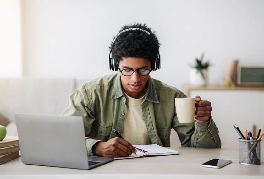 student with headphones, laptop and notebook, studying with coffee mug