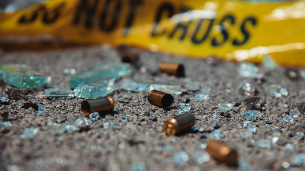 bullet casings on concrete surrounded by broken glass and yellow police tape