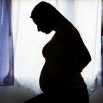 shadowed pregnant woman in front of curtained window