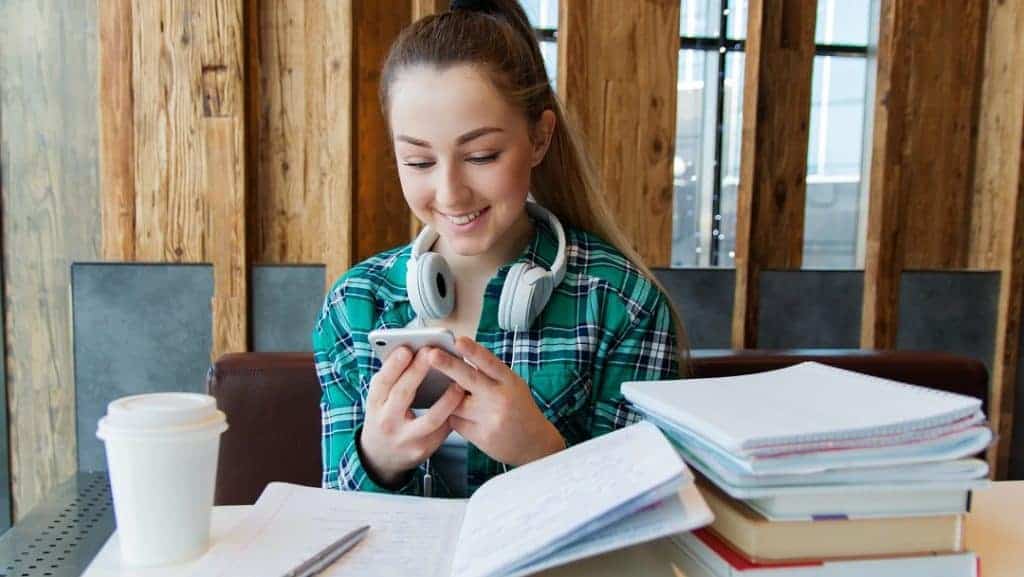 female student studying with smartphone, headphones, notebook