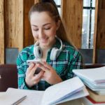 female student studying with smartphone, headphones, notebook